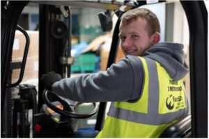 A FareShare worker in a safety vest is seated in a forklift's driver's seat. Photo credit: FareShare Thames Valley/SOFEA